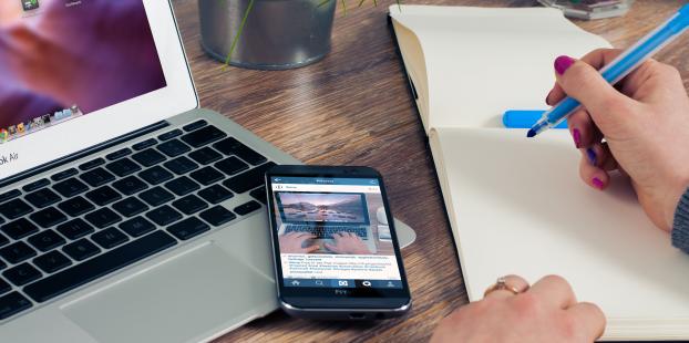 Person writing at desk in front of laptop