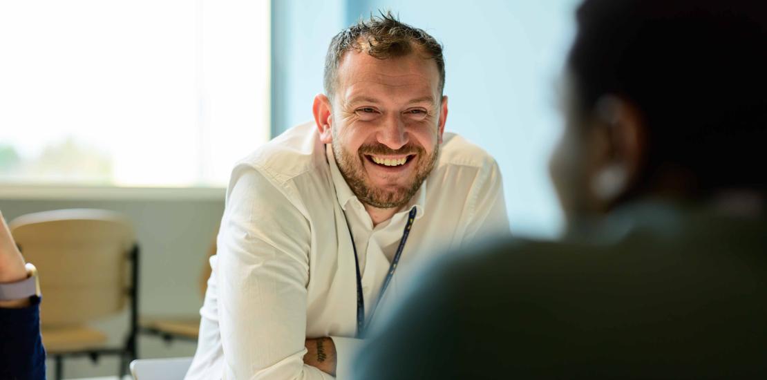 A man smiling in conversation with a colleague